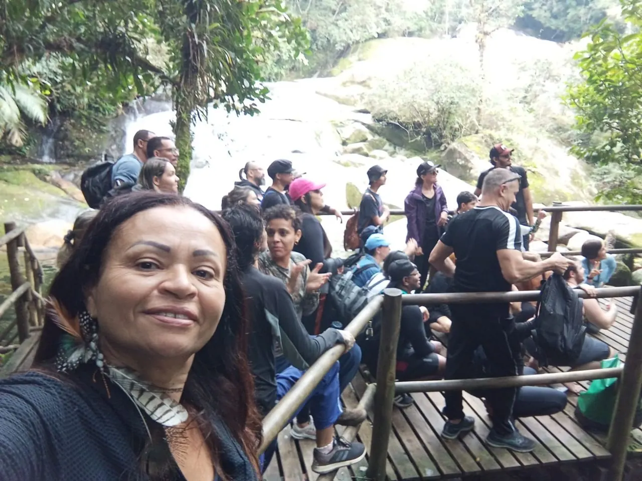 Grupo grande em passarela de madeira junto a uma cachoeira na mata